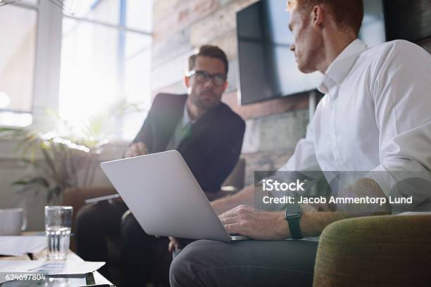 Hombre De Negocios Con Computadora Portátil Hablando Con Su Colega Durante La Reunión Foto de stock y más banco de imágenes de Enfoque diferencial