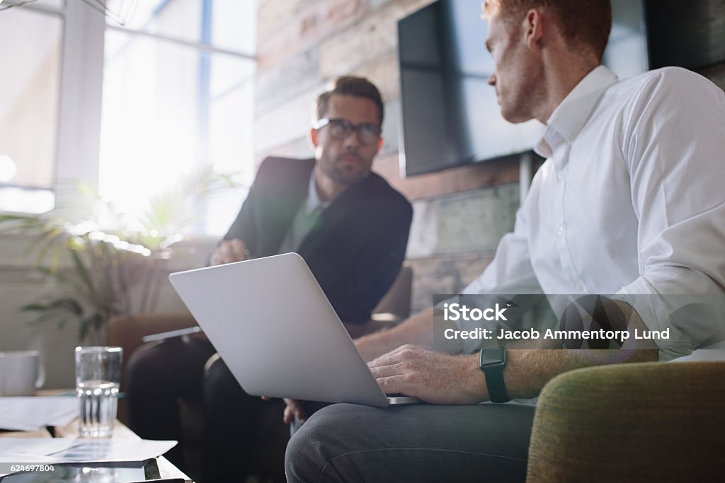 Businessman with laptop talking with colleague during meeting Two young man sitting in office and discussing business. Businessman with laptop talking with colleague during meeting. Selective Focus Stock Photo