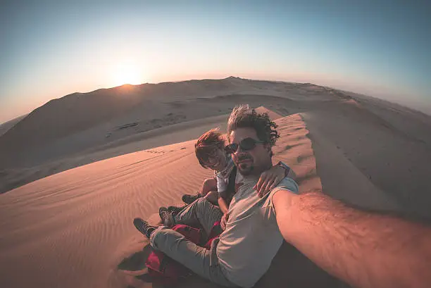 Adult couple taking selfie on sand dunes in the Namib desert, Namib Naukluft National Park, main travel destination in Namibia, Africa. Fisheye view in backlight, toned image.