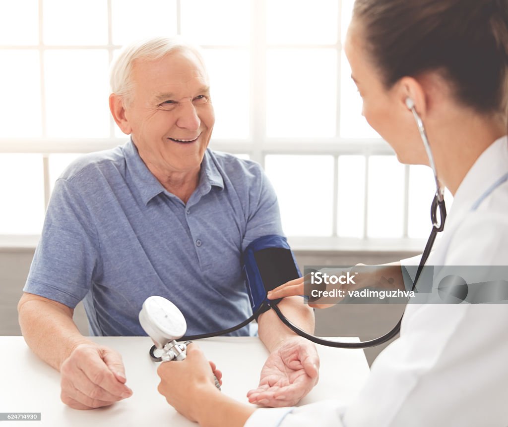 Beautiful doctor and patient Handsome old man is having his blood pressure tested and smiling while sitting at the doctor's General - Military Rank Stock Photo