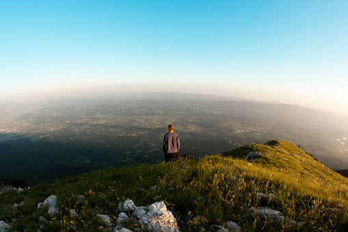 A young man looking at the valley on the top of a hill in sunset time.