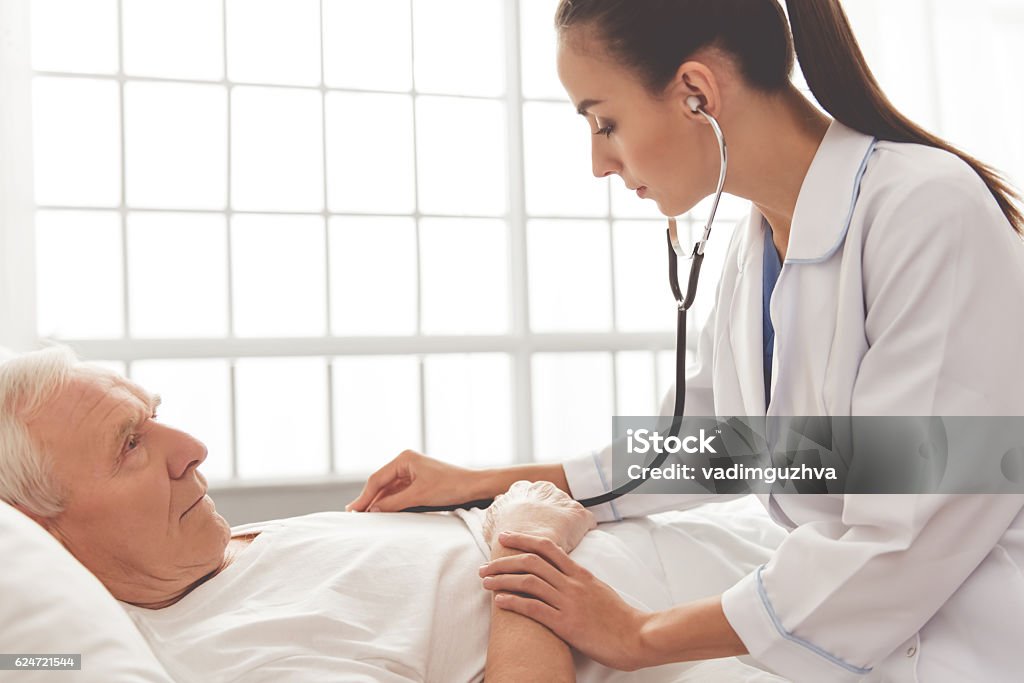 Old man in hospital Beautiful female doctor in white medical coat is checking her old patient's heart and lungs using a stethoscope Doctor Stock Photo