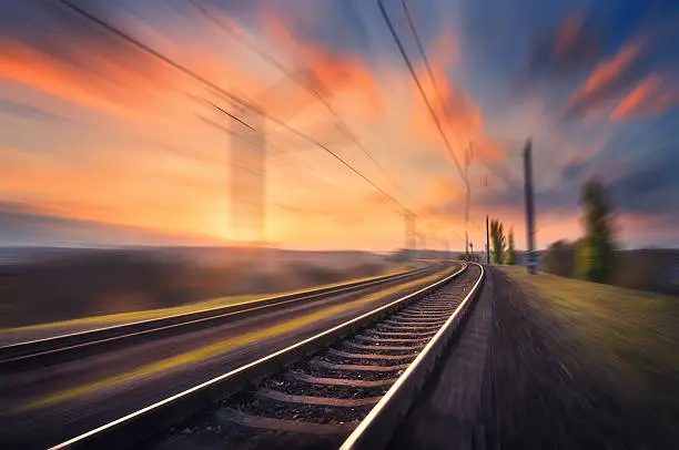 Railroad in motion at sunset. Railway station with motion blur effect against colorful blue sky, Industrial concept background. Railroad travel, railway tourism. Blurred railway. Transportation