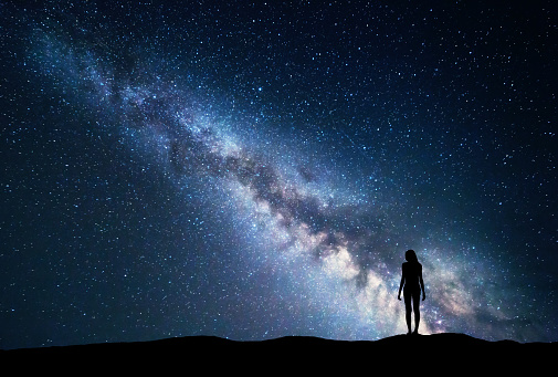 Milky Way with standing woman. Colorful landscape with night sky with stars and silhouette of a girl on the mountain on the background of beautiful galaxy. Blue milky way. Travel. Bright stars