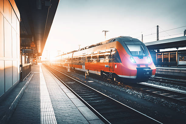 Modern high speed red commuter train at the railway station Modern high speed red commuter train at the railway station at sunset. Turning on train headlights. Railroad with vintage toning. Train at railway platform. Industrial landscape. Railway tourism railroad station platform stock pictures, royalty-free photos & images
