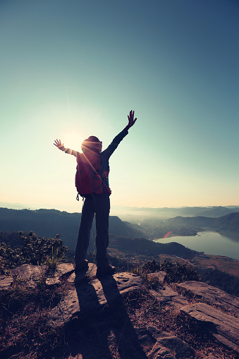 cheering young woman hiker open arms to the sunrise