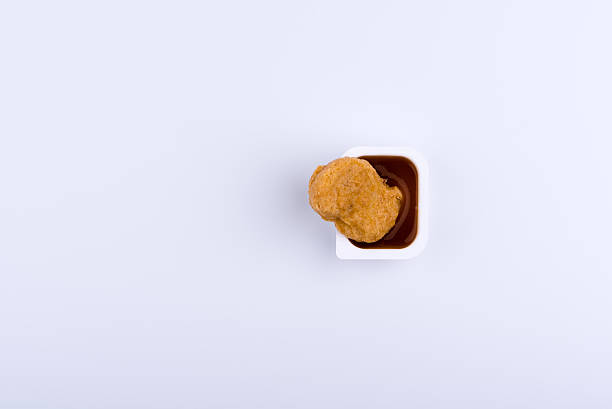 istock Single chicken nugget standing in red dip sauce 624750092