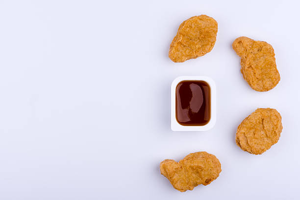 Dip sauce in plastic container and by four chicken nuggets Red dip sauce in plastic container surrounded by four chicken nuggets which form a half circle, isolated on white background nuggets heat stock pictures, royalty-free photos & images