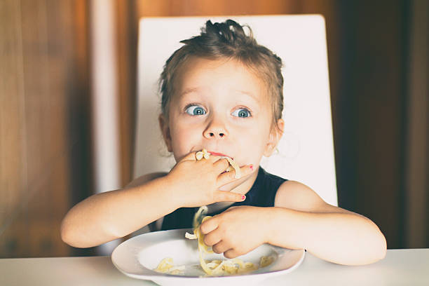 Little girl eating pasta Three years old girl sitting at the table in the kitchen and eating pasta. kids eating noodles stock pictures, royalty-free photos & images