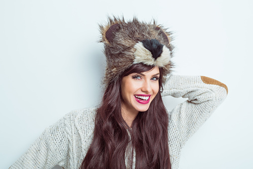 Winter portrait of beautiful young woman wearing a bear head fur hat and sweater. White background. Studio shot.