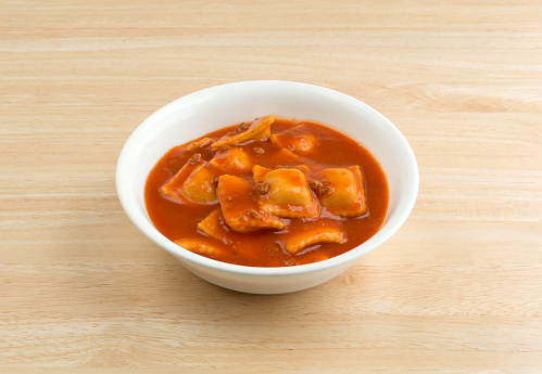 A serving of ravioli in a white bowl on a wood table.