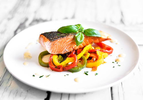 Delicious salmon filet with decorative basil leaf and multicolored paprika or bell pepper vegetable. Healthy eating scene.