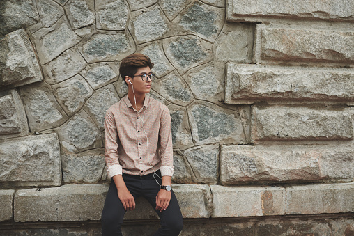 Young man in earphones sitting at stone wall