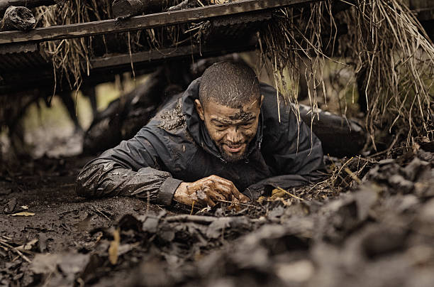 泥の実行中に障害物の下に登る黒いハンサムな若者 - 這う　男性 ストックフォトと画像