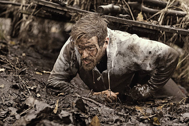 caucasian blonde handsome man crawling under obstacle during mud run - mud run imagens e fotografias de stock