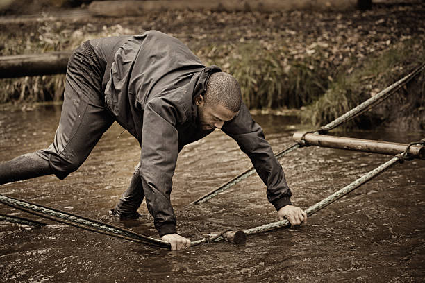 Black handsome young man climbing over obstacle during mud run
