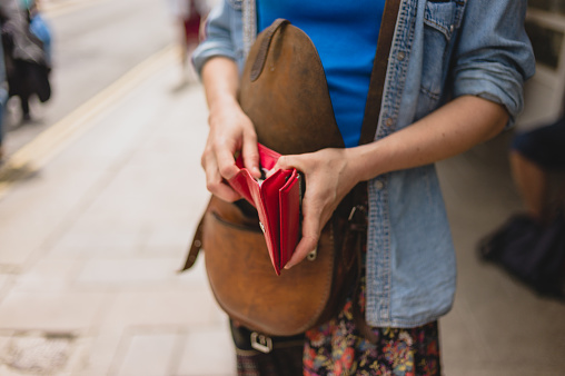 A young woman is standing in the street and is opening her purse to make a purchase