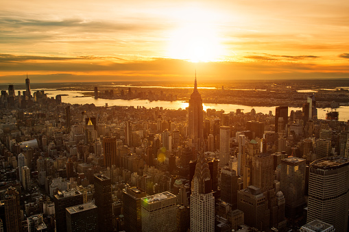 Helicopter point of view of New York City skyscrapers. Empire State building and many details are visible in the image. Sunset is in the background.