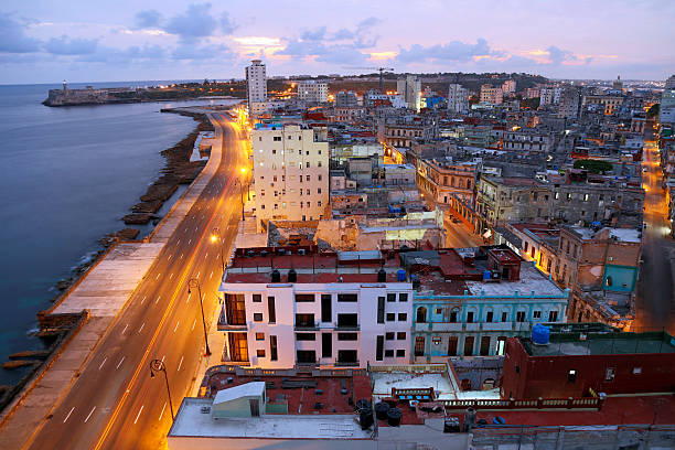 Havana, Cuba illuminated at early morning, elevated view Elevated view of Havana, Cuba at early morning before sunrise, the famous Malecon seaside promenade is visible on the left. The Castillo de los Tres Reys del Morro, commonly known as El Morro can be seen in the background left, lights from  buildings and streets glow, HDR image. morro castle havana stock pictures, royalty-free photos & images