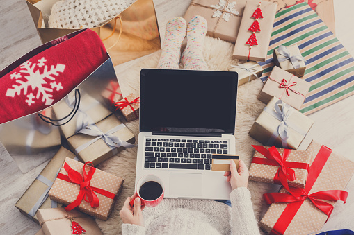 Christmas online shopping top view. Female buyer with laptop, copy space on screen. Woman buys presents in internet with gold credit card, drinks coffee among gift boxes. Winter holidays sales