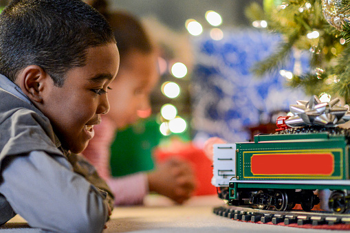 A brother and sister are playing with a toy train on Christmas morning.