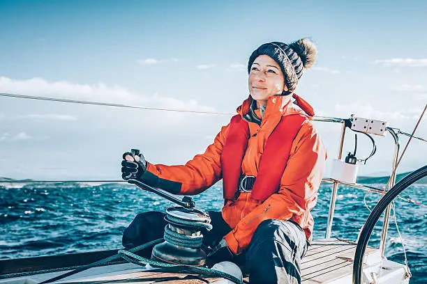 Happy woman sailor sailing as main sail trimmer during regatta.