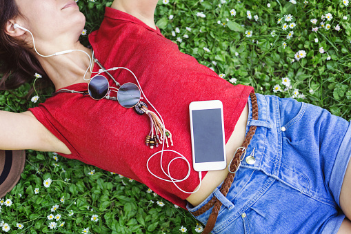Brunette girl listening to music, and lying down on a lawn with daisies. Creative crop - no face.