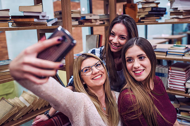 istock Group of smiling female students taking selfie at school library 624898042
