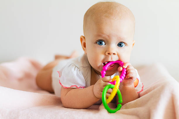 Baby girl with teething ring Little girl lying and biting teether. only baby girls stock pictures, royalty-free photos & images
