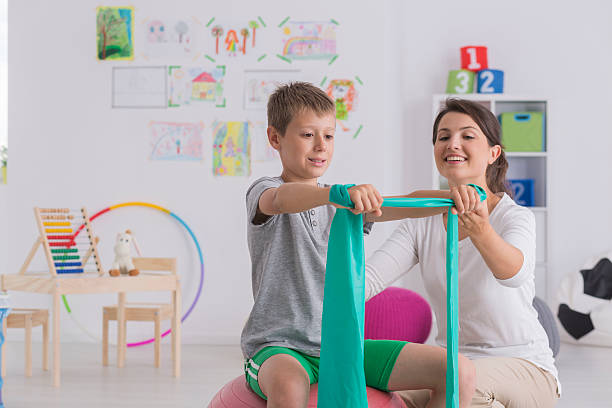 Physiotherapist and boy sitting on a gym ball Physiotherapist and boy sitting on a gym ball exercising with a rubber tape physiotherapy stock pictures, royalty-free photos & images