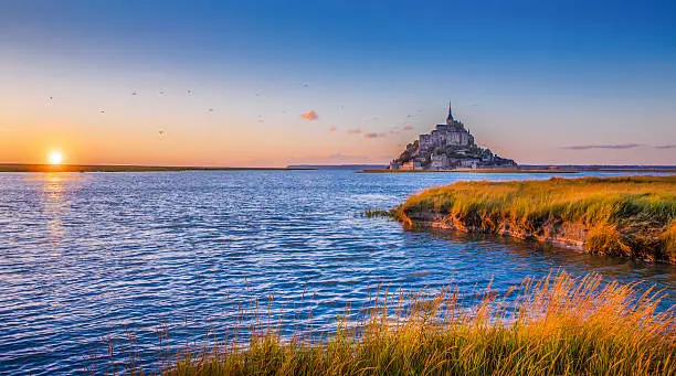 Panoramic view of famous Le Mont Saint Michel tidal island in beautiful golden evening light at sunset in summer, Normandy, France.