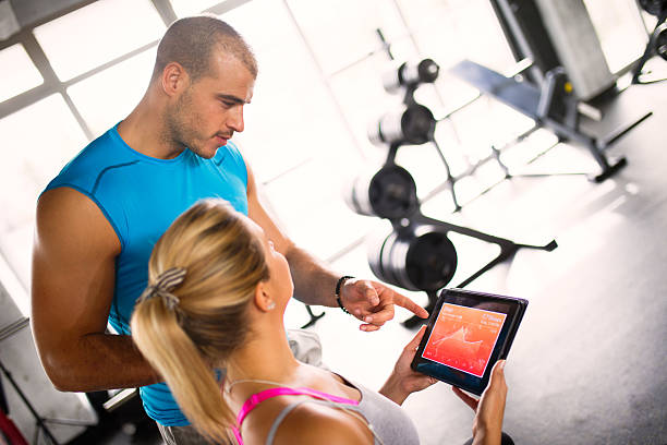 istock Young woman discussing workout progress with fitness instructor 624912426