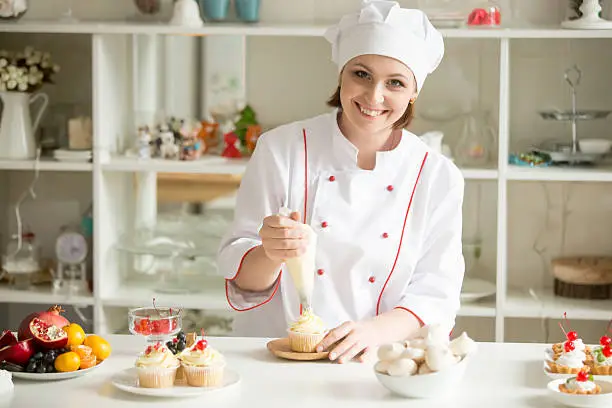 Photo of Portrait of female confectioner topping a cupcake with cream