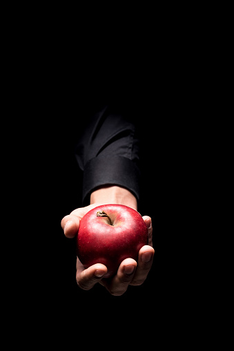 Delicious fruit. Close up of mans hand holding a red big apple and standing on black background while demonstrating it.