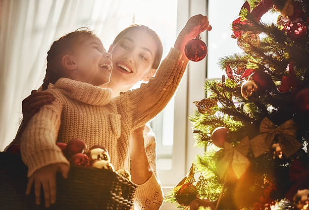 Mom and daughter decorate the Christmas tree Merry Christmas and Happy Holidays! Mom and daughter decorate the Christmas tree indoors. The morning before Xmas. Portrait loving family close up. family christmas stock pictures, royalty-free photos & images