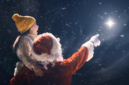 Merry Christmas and happy holidays! Cute little child girl and Santa Claus looking at Christmas star. Christmas legend concept.