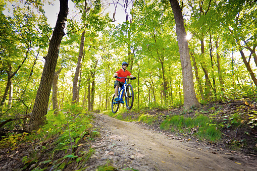 Mountain biker in a wildness biking trail in the midwest of USA. He is a Caucasian young man riding a mountain bike in the late afternoon. Photographed on location in horizontal format.