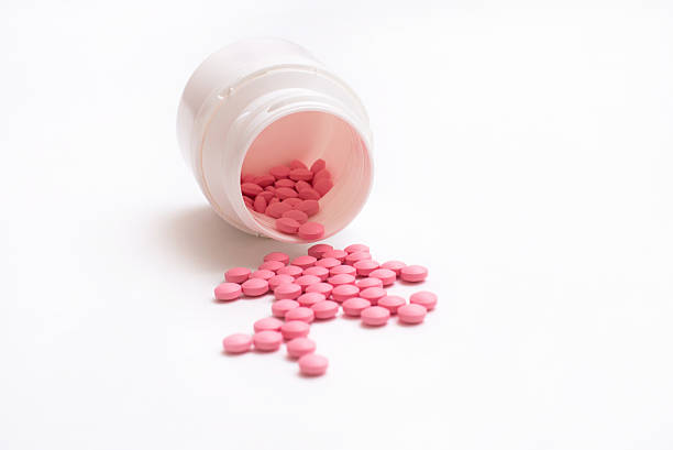istock Pink pills spill out from bottle isolated on white background. 624959114