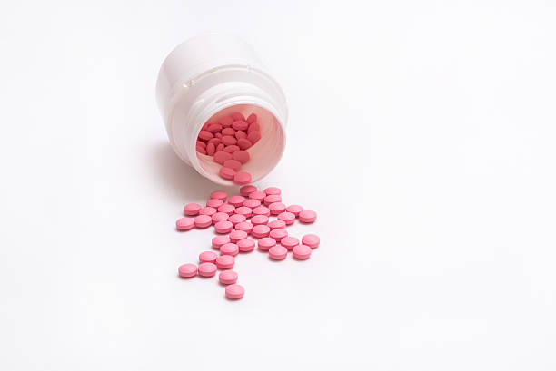 istock Pink pills spill out from bottle isolated on white background. 624959416