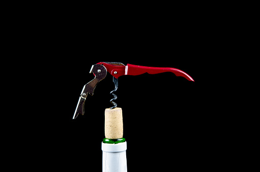 Wine bottle top with a red metal corkscrew in the cork at a black background
