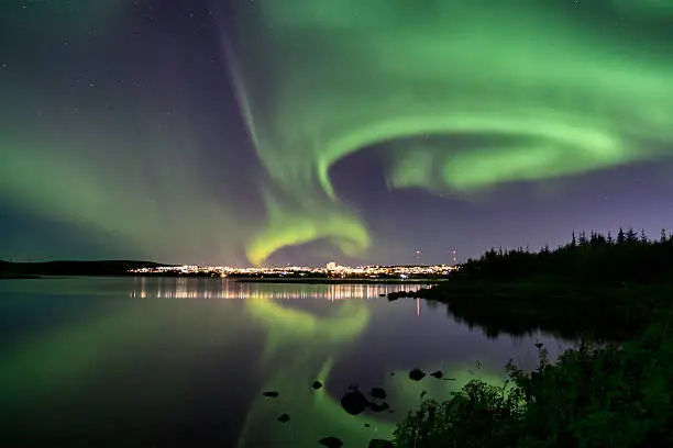 Auroras over Eillidavatn close to Reykjavik in Iceland. calm water reflecting the northern lights blazing in the sky.