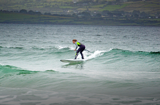 Woman surfing wave on stand-up-paddleboard in Kerry, Ireland. 