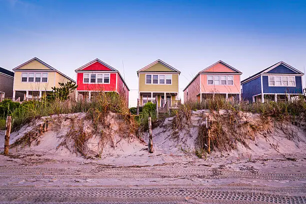 A summer scene on the beach with cottages in a line.