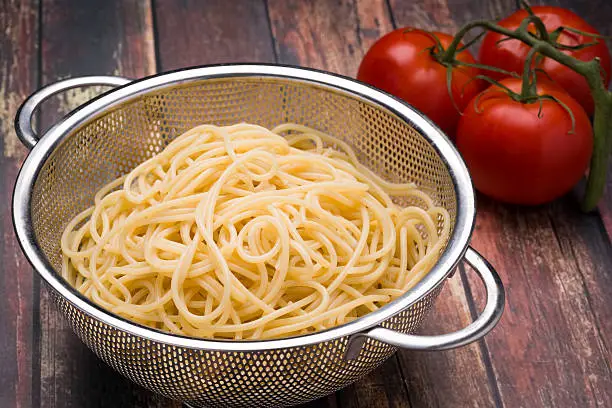 Spaghetti in a stainless steel collander on a wood surface