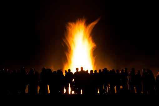 Long exposure of people watching a bonfire at night, slight motion blur to people and the fire