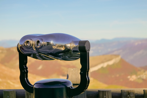 Coin operated binocular against mountains and warm sky in Italy. Observation and wildlife watching concept