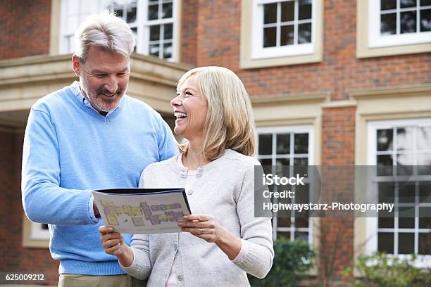 Mature Couple Standing Outside House Looking At Property Details Stock Photo - Download Image Now