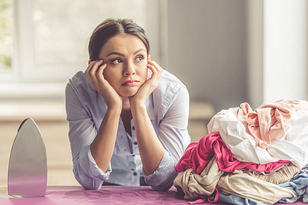 Woman ironing clothes Beautiful bored young woman is leaning on ironing board and looking away while ironing clothes at home iron appliance photos stock pictures, royalty-free photos & images