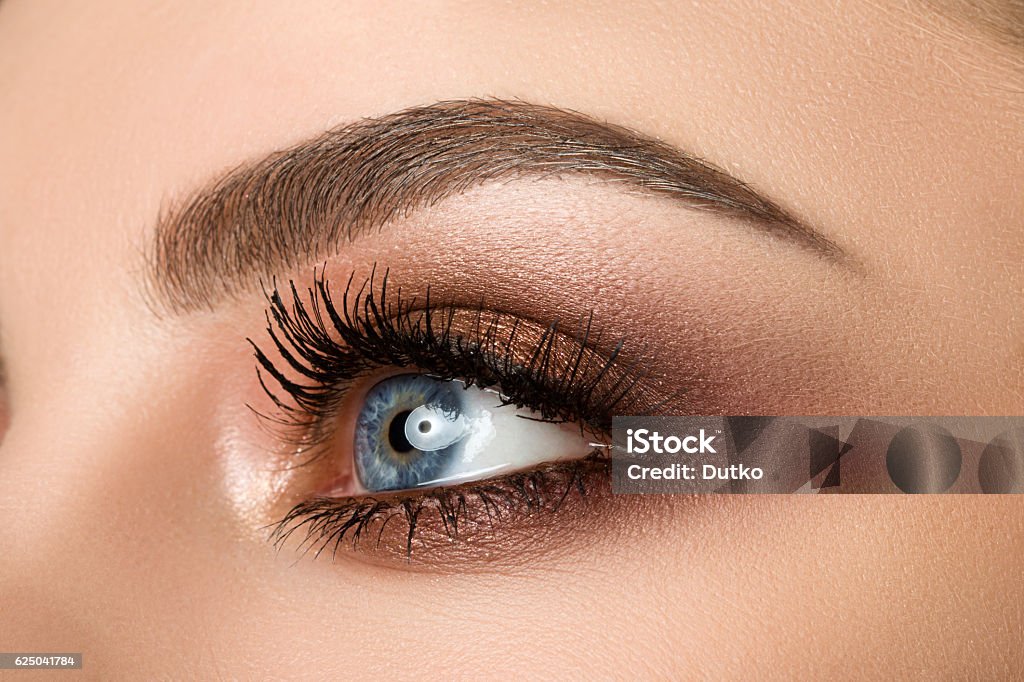 Close-up of woman eye with beautiful brown smokey eyes makeup Close up of blue woman eye with beautiful brown with red and orange shades smokey eyes makeup. Modern fashion make up. Eyebrow Stock Photo