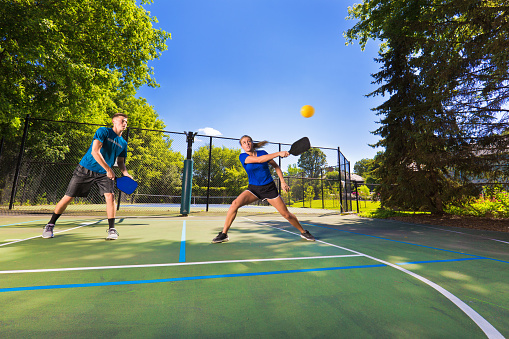 A Caucasian young woman and a young man playing double in pickleball in a pickleball court. Pickleball, one of the faster growing sport in the United States. Photographed in action in horizontal format.